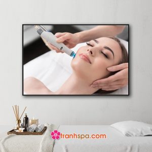 Mẫu tranh trang trí spa đẹp hình ảnh nữ khách hàng đang được chăm sóc da mặt bằng thiết bị công nghệ cao