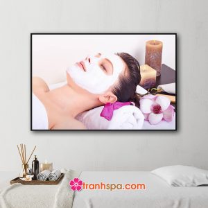 Mẫu tranh treo spa đẹp hình ảnh cô gái nằm đắp mặt nạ trong không gian được trang trí với hoa và nến thơm