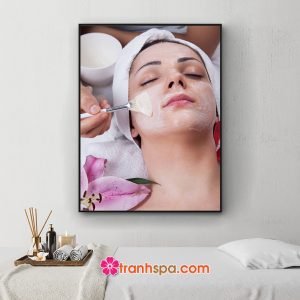 Mẫu tranh treo spa đẹp hình ảnh nữ khách hàng đang nằm thư giãn để nhân viên thẩm mỹ viên chăm sóc da mặt