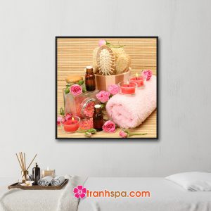 Mẫu tranh trang trí spa đẹp khổ vuông hình ảnh hoa hồng, khăn tắm màu hồng, nến thơm hồng, muối tắm, tinh dầu và dụng cụ...trên nền mành trúc