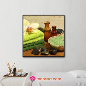 Mẫu tranh trang trí spa đẹp khổ vuông hình ảnh chai tinh dầu, muối tắm màu xanh, hoa lan và khăn tắm, đá cuội đen bóng đặt trên nền trúc