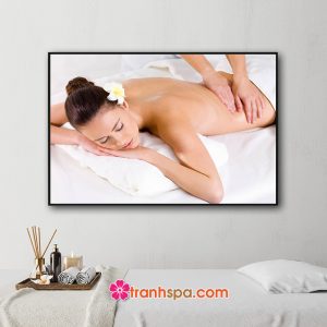 Mẫu tranh trang trí spa đẹp hình ảnh nữ khách hàng cài hoa sứ trên tóc đang nằm massage thư giãn trên nền màu trắng muốt của ga giường và khăn tắm
