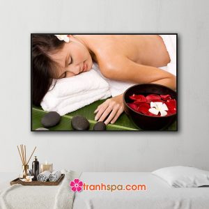 Mẫu tranh treo spa đẹp hình ảnh nữ người mẫu đang nằm thư giãn, bên cạnh là bát nước rải cánh hoa hồng đỏ và hoa sứ trắng cùng những viên đá cuội đen trên tàu lá chuối xanh