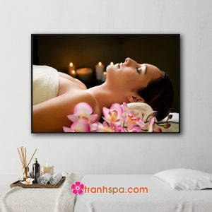 Mẫu tranh treo spa đẹp hình ảnh cô gái đang nằm thư giãn trong phòng spa với cành hoa lan bên cạnh và những ngọn nến thơm