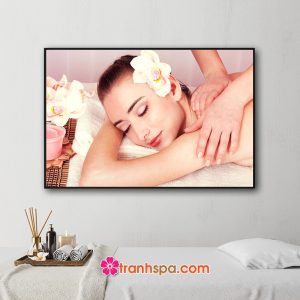 Mẫu tranh treo spa đẹp hình ảnh nhân viên đang massage vai cho nữ khách hàng với hoa lan cài tóc và nến thơm