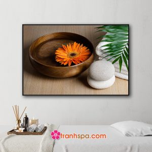 Mẫu tranh trang trí spa đẹp hình ảnh bông hoa cúc vàng cam thả tron bát nước trong, lá dừa xanh, khăn tắm và đá cuội đặt trên nền gỗ