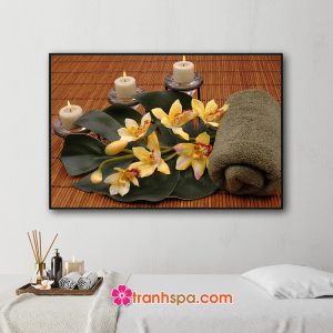 Mẫu tranh trang trí spa đẹp hình ảnh khăn tắm cuộn, cành phong lan vàng, lá trầu bà và nến thơm đặt trên chiếu trúc