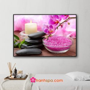 Mẫu tranh trang trí spa đẹp với gam màu tím hồng của cành phong lan, khăn tắm, bát muối hồng, nến thơm và đá cuội đặt trên nền mành trúc