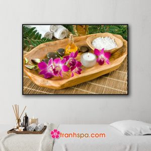 Mẫu tranh trang trí spa đẹp hình ảnh khăn tắm, tinh dầu và lá xanh, khay gỗ đựng hoa lan, nến thơm, đá cuội và bát muối tắm đặt trên mành trúc