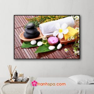 Mẫu tranh trang trí spa đẹp hình ảnh khay khăn tắm, đá cuội, soap, tinh dầu, muối tắm, đá tròn trắng và các loại hoa đẹp đặt trên nền mành gỗ sơn màu nâu